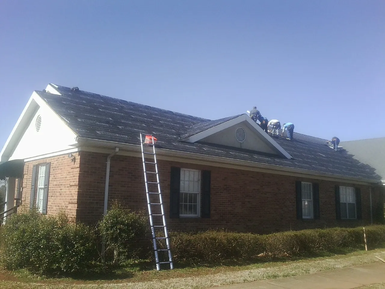 Crew tearing shingles off a brick ranch roof with a ladder set — Metal Roof Repair work by our crew in Otisville