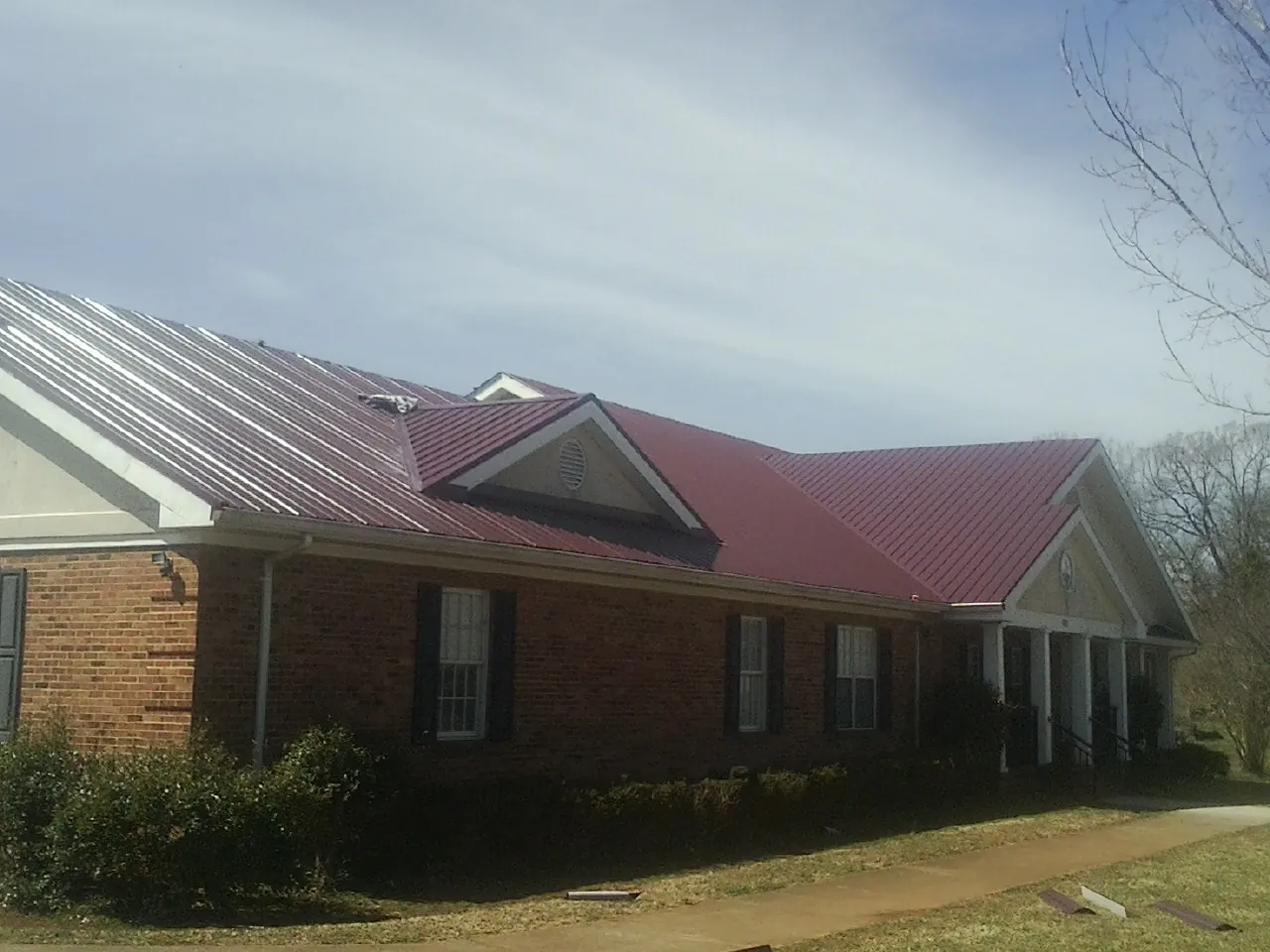Red metal roof with gabled entries on a long brick building, from a Hail Damage Roof Repair job in Otisville