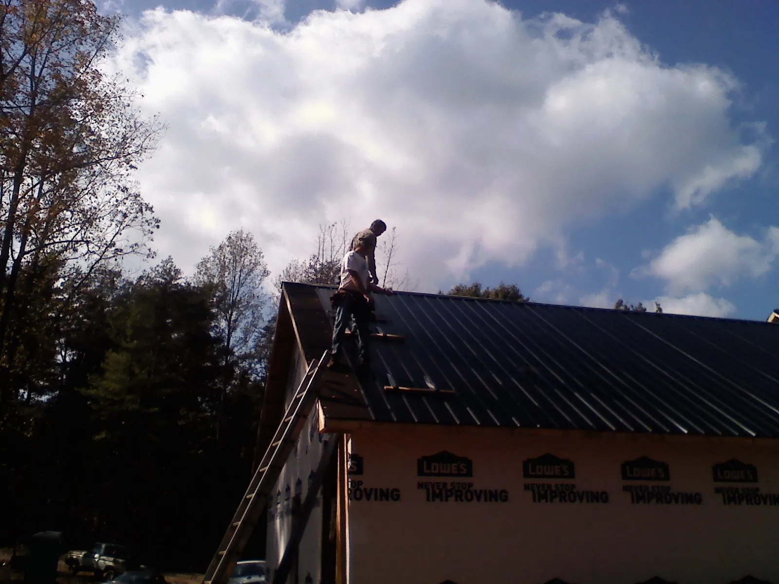 Roofer fastening dark metal panels high against a cloudy sky, from a Roof Inspection job in Otisville