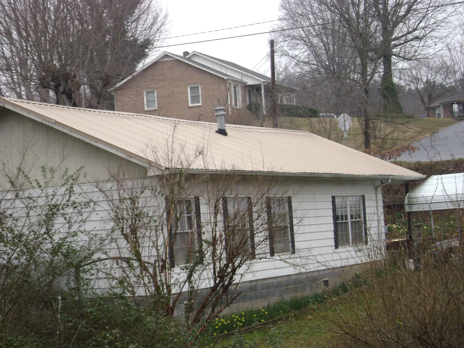 Tan metal roof on a white sided house set into a hillside — Commercial Roofing by Roofing Brothers in Otisville